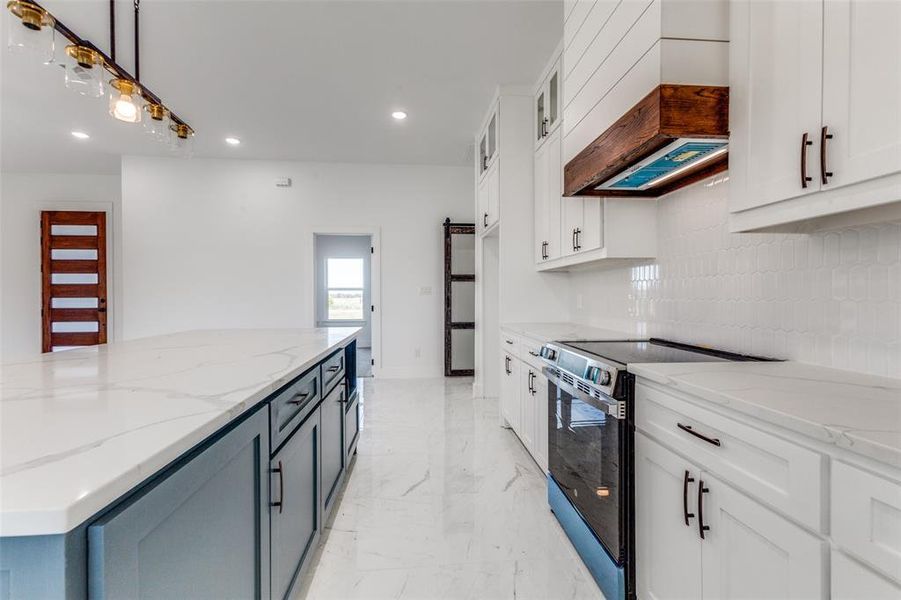 Kitchen featuring electric range, white cabinets, hanging light fixtures, and custom range hood