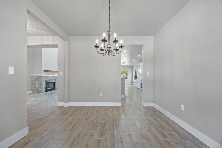 Unfurnished dining area with a fireplace, light wood-style flooring, baseboards, and an inviting chandelier Unfurnished dining area with a fireplace, light wood-style flooring, baseboards, and an inviting chandelier