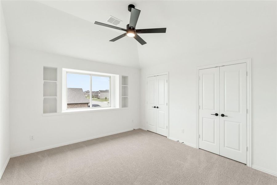 Empty bedroom with vaulted ceiling, ceiling fan, built-in shelves, and two white double doors Empty bedroom with vaulted ceiling, ceiling fan, built-in shelves, and two white double doors
