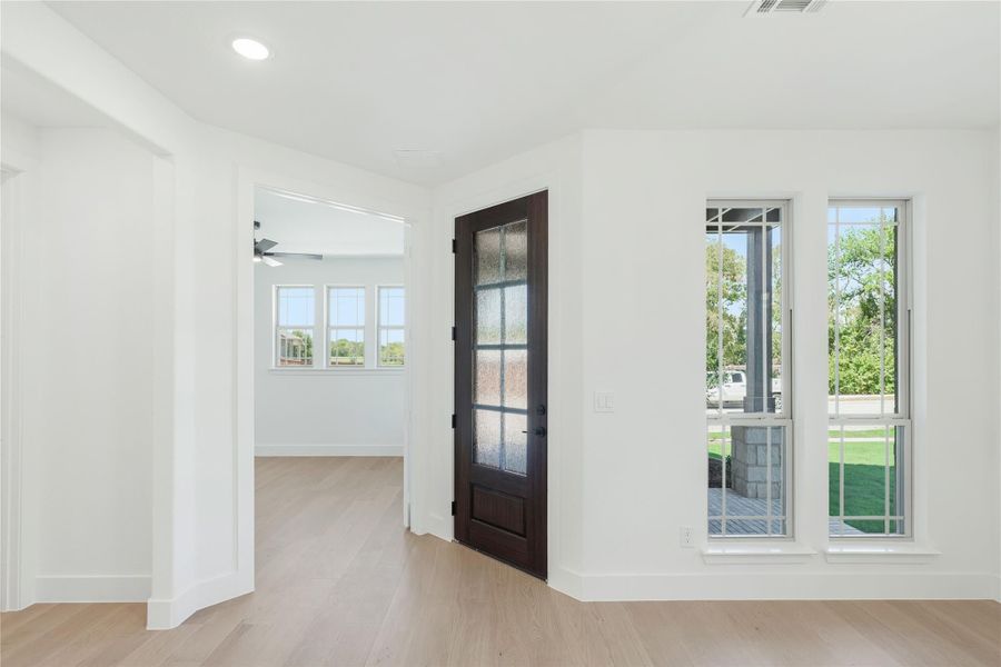 Bright entryway with dark wood glass-panel door, white walls, and light hardwood floors leading to an open room. Bright entryway with dark wood glass-panel door, white walls, and light hardwood floors leading to an open room.