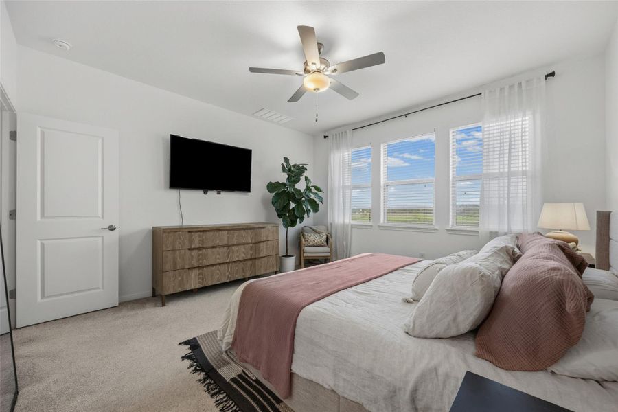 Light-filled room featuring three large windows with white blinds, neutral carpeting, a white two-panel door, and a ceiling fan with integrated lighting