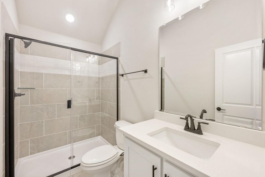 Bathroom with glass-enclosed tiled shower, white vanity with black fixtures, and vaulted ceiling
