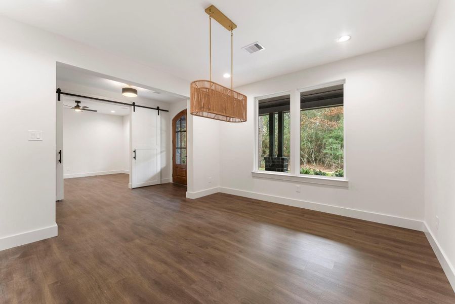 Another view of the dining room showcasing the modern light fixture and a sliding barn door  leading to an adjacent study, adding a stylish touch.