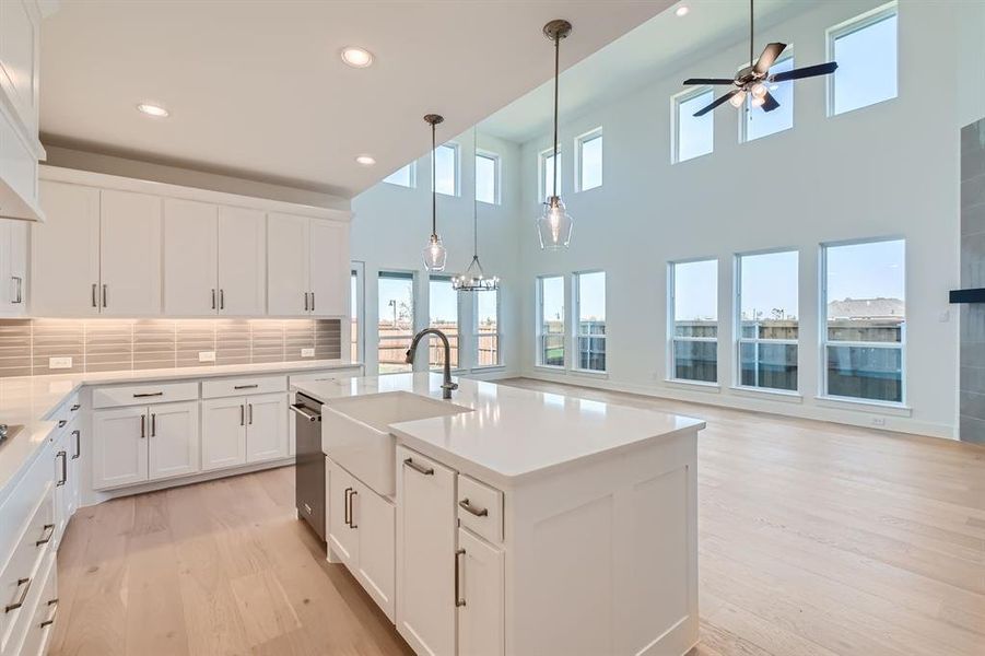 Kitchen with sink, light wood-type flooring, an island with sink, hanging light fixtures, and white cabinetry