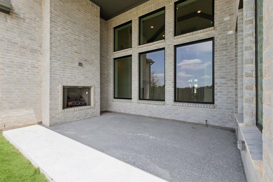Covered outdoor patio featuring light-colored brick exterior, a built-in outdoor fireplace, and multiple floor-to-ceiling windows with black frames Covered outdoor patio featuring light-colored brick exterior, a built-in outdoor fireplace, and multiple floor-to-ceiling windows with black frames