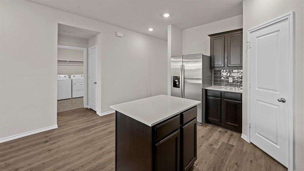 Kitchen with stainless steel fridge with ice dispenser, dark wood-type flooring, washer and clothes dryer, dark wood finish cabinetry, and a center island