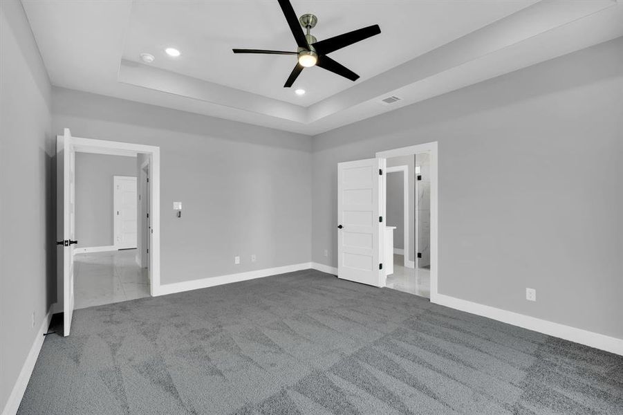 Unfurnished bedroom featuring ceiling fan, carpet flooring, and a tray ceiling