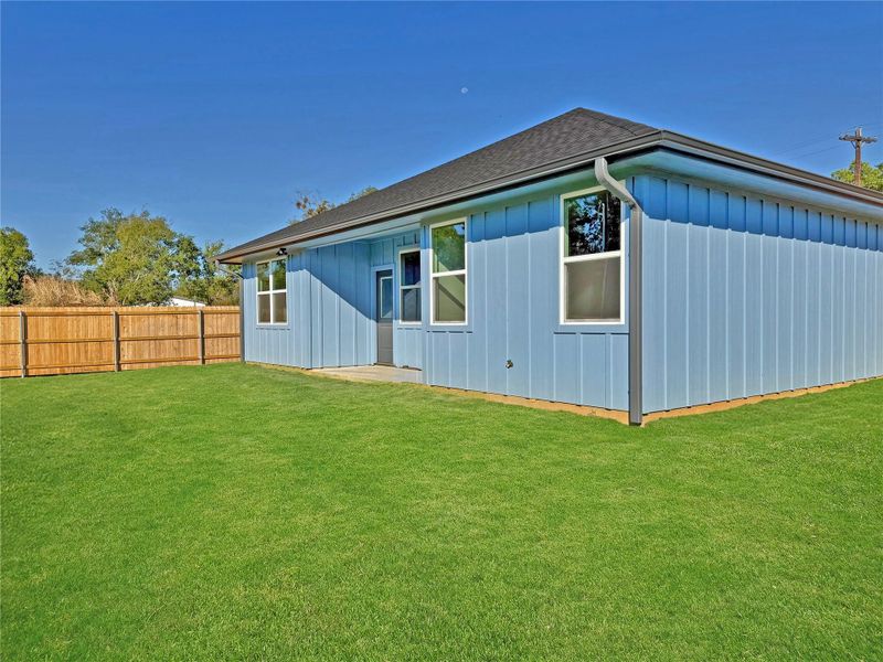 Back of house featuring board and batten siding and roof with shingles.This image enhanced by AI to showcase the newly installed carpet grass.