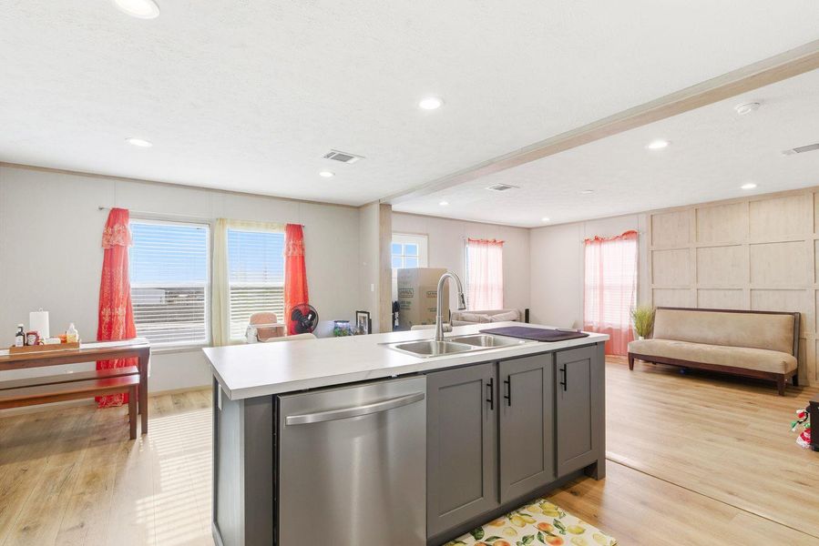Kitchen with stainless steel dishwasher, open floor plan, a center island with sink, light wood-type flooring, and light countertops