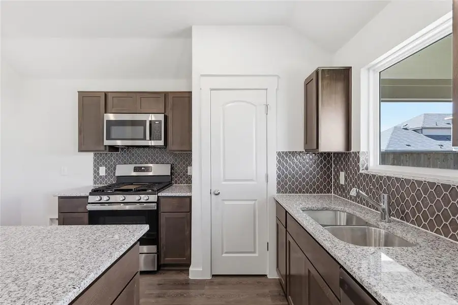 Kitchen with stainless steel appliances, light stone countertops, dark wood-style floors, dark wood finish cabinetry, and lofted ceiling