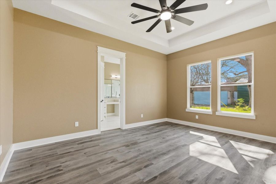 The spacious primary bedroom offers an 11-foot tray ceiling, complemented by recessed lighting and a ceiling fan. Two windows provide natural light, and an 8-foot door leads to the en-suite bathroom.