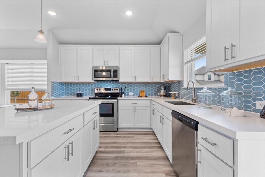 Kitchen with appliances with stainless steel finishes, a sink, light countertops, white cabinetry, and recessed lighting Kitchen with appliances with stainless steel finishes, a sink, light countertops, white cabinetry, and recessed lighting