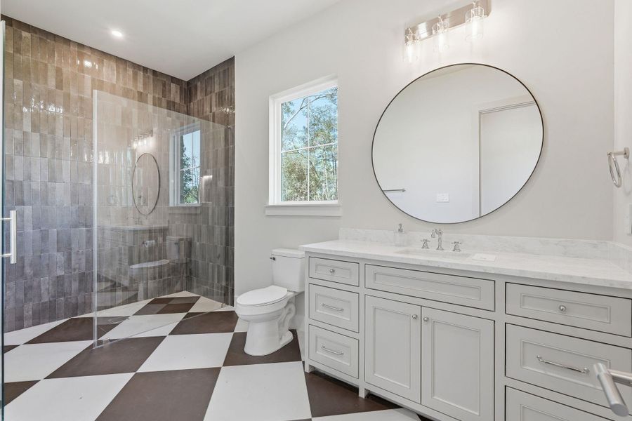 Designer guest bathroom with aglass-enclosed shower, dramatictile floors and an oversizedvanity topped in marble.