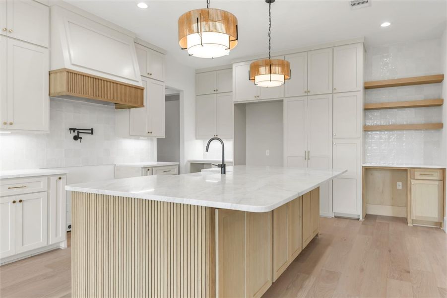 Dual tone kitchen featuring backsplash, a kitchen island with sink, light wood-style floors, light stone countertops, and decorative light fixtures
