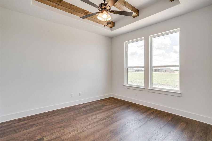 Spare room featuring a tray ceiling, beam ceiling, ceiling fan, and dark wood-type flooring