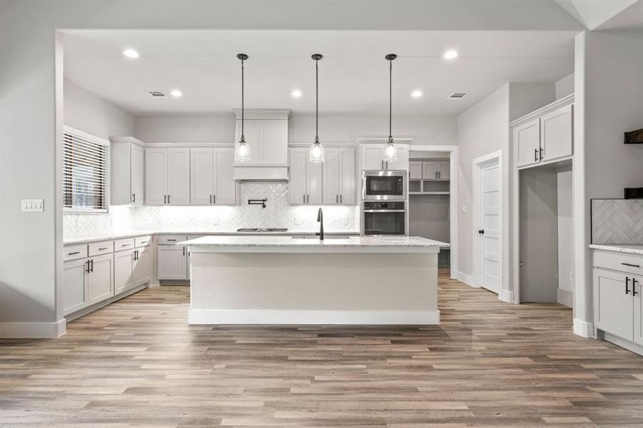 Kitchen featuring an island with sink, light hardwood / wood-style floors, decorative light fixtures, and appliances with stainless steel finishes