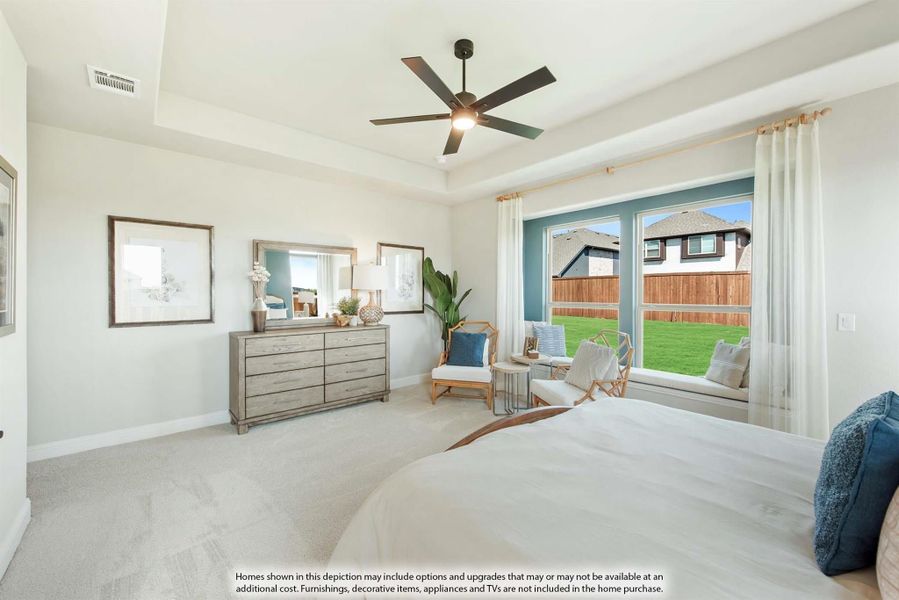 Bedroom with tray ceiling, ceiling fan, carpet flooring, wood dresser, and large windows overlooking backyard Bedroom with tray ceiling, ceiling fan, carpet flooring, wood dresser, and large windows overlooking backyard