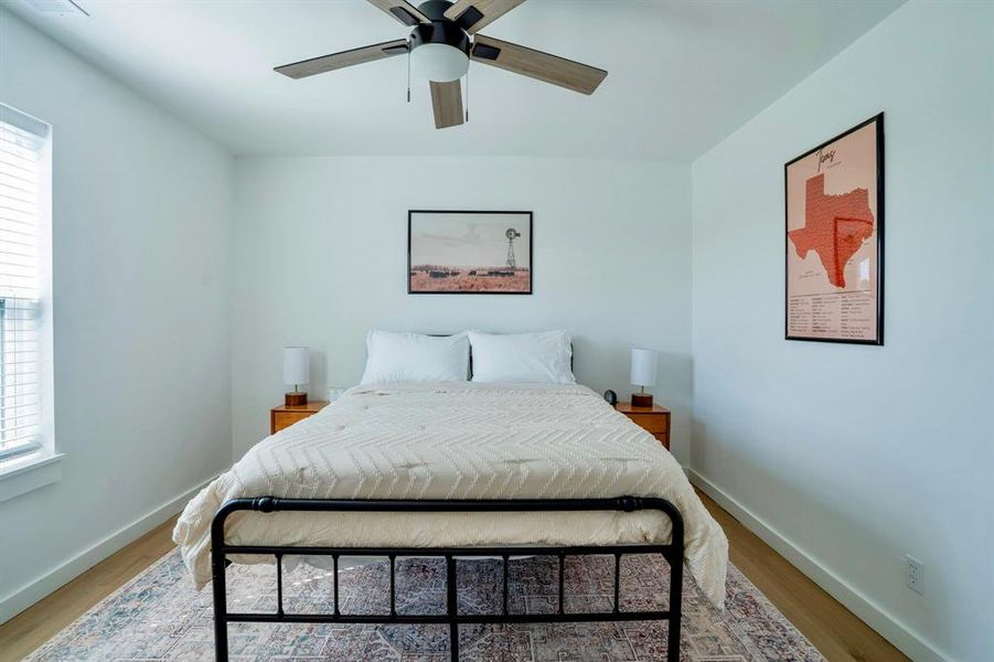 This bedroom features light wood flooring, a ceiling fan with integrated lighting, and a window with blinds