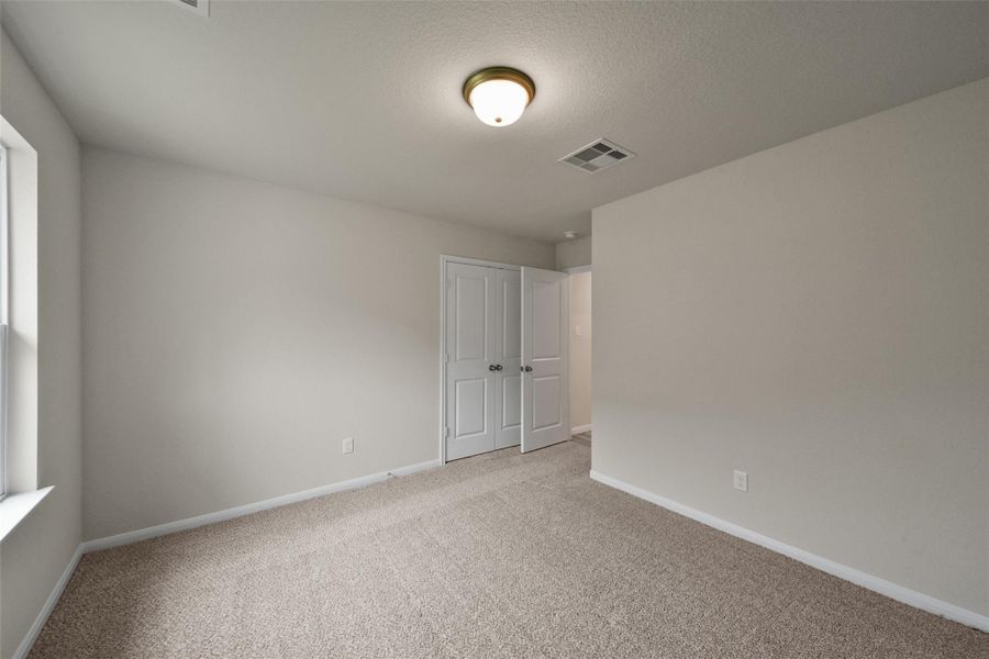 Bright, carpeted room featuring a double-door closet, neutral tones, and ample natural light.