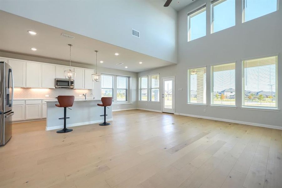 Unfurnished living room with light wood finished floors, recessed lighting, ceiling fan, and a high ceiling Unfurnished living room with light wood finished floors, recessed lighting, ceiling fan, and a high ceiling