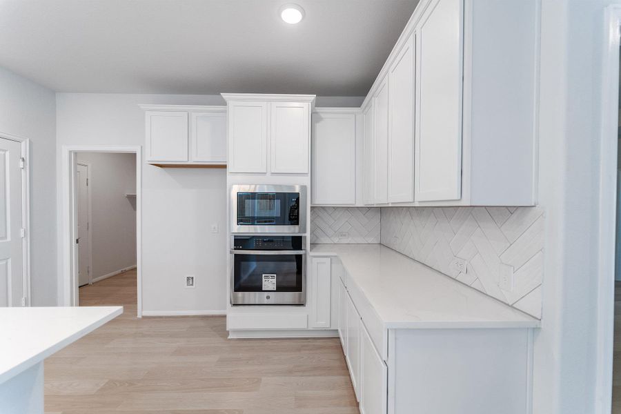 Kitchen featuring white cabinets, light wood-type flooring, stainless steel appliances, light stone countertops, and backsplash