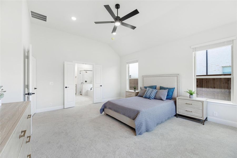 Spacious master bedroom with vaulted ceiling, ceiling fan, carpet floors, and ensuite bathroom doorway Spacious master bedroom with vaulted ceiling, ceiling fan, carpet floors, and ensuite bathroom doorway