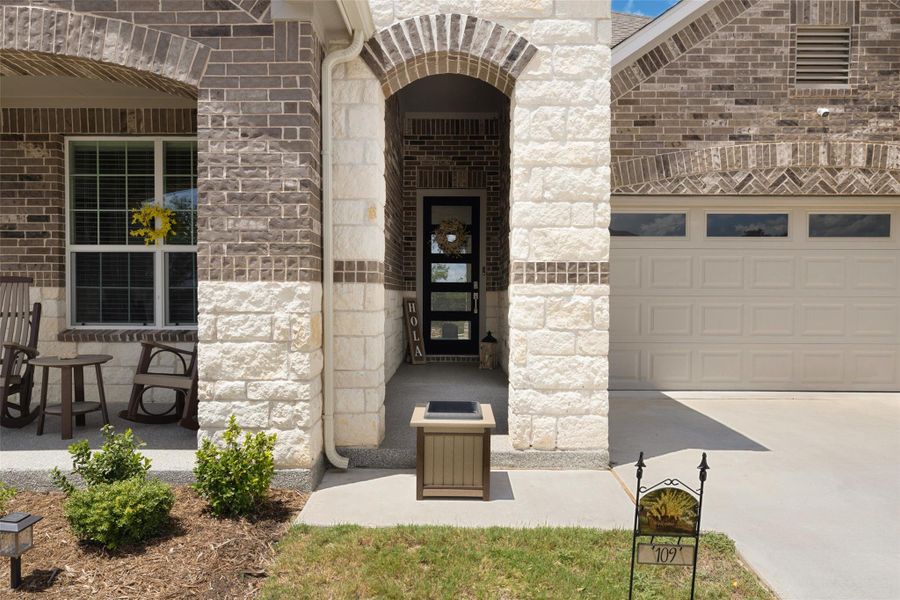 Property entrance featuring stone siding, an attached garage, driveway, and brick siding Property entrance featuring stone siding, an attached garage, driveway, and brick siding