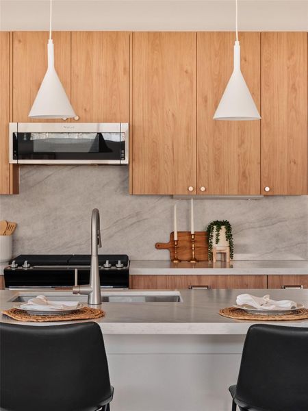 Kitchen with a kitchen breakfast bar, stainless steel microwave, modern cabinets, hanging light fixtures, and decorative backsplash