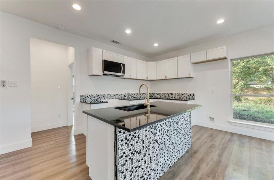 Kitchen with sink, white cabinets, light hardwood / wood-style floors, and an island with sink