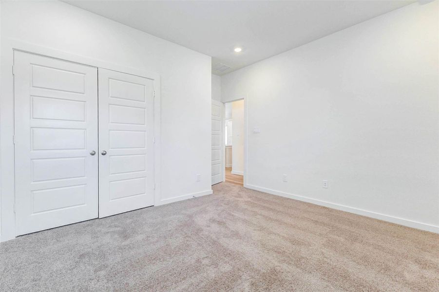 Secondary bedroom view showcasing soft carpet, neutral paint, recessed lighting, and double closet doors. The simple, bright finish makes the room easy to personalize and provides a functional layout for a variety of furniture arrangements.