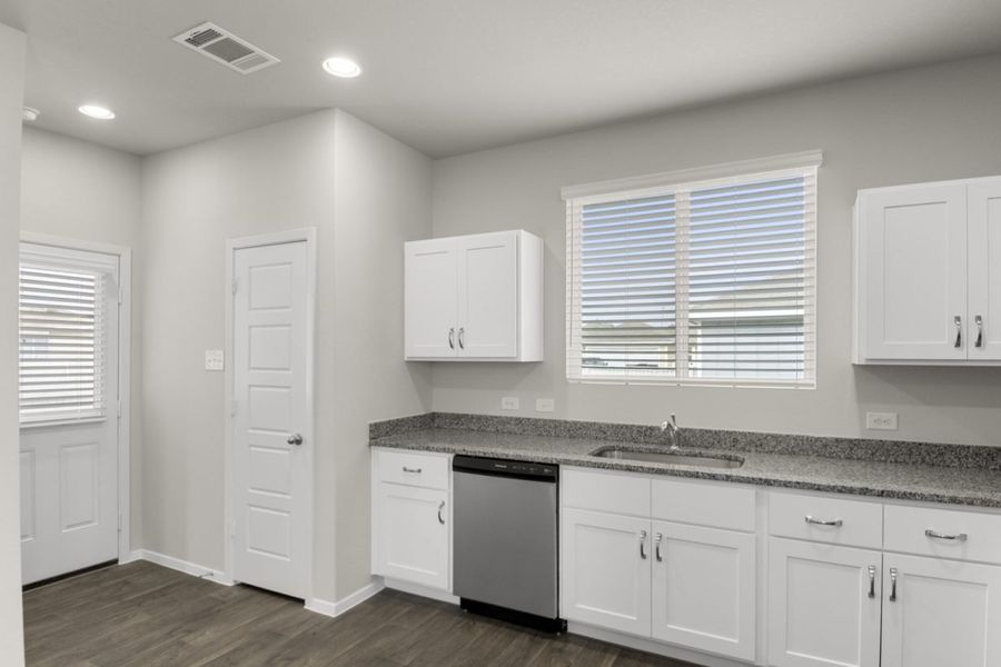 Image of a kitchen with white cabinets, stainless steel dishwasher, a window above the sink and a back door with a window