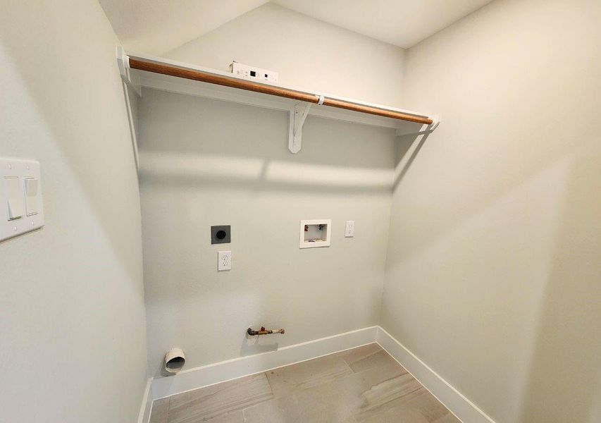 This photo shows a compact laundry room with washer and dryer hookups, a shelf for storage, and light-colored walls and flooring. This photo shows a compact laundry room with washer and dryer hookups, a shelf for storage, and light-colored walls and flooring.