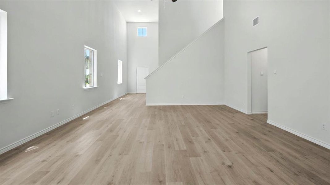 Unfurnished living room featuring light wood-type flooring, a towering ceiling, and a ceiling fan