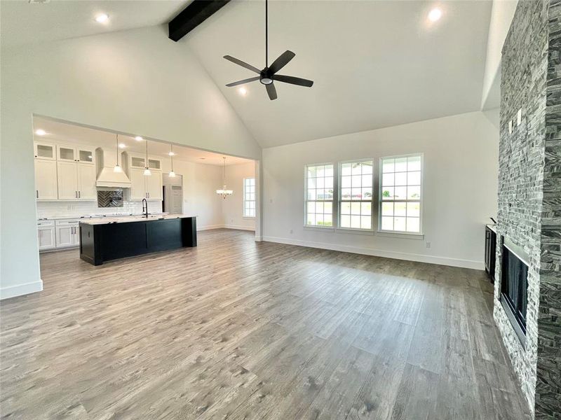 Unfurnished living room featuring a sink, beamed ceiling, ceiling fan with notable chandelier, a stone fireplace, and high vaulted ceiling Unfurnished living room featuring a sink, beamed ceiling, ceiling fan with notable chandelier, a stone fireplace, and high vaulted ceiling