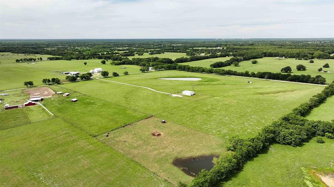 Expansive agricultural property featuring multiple structures, open pastures, tree lines, and two visible ponds