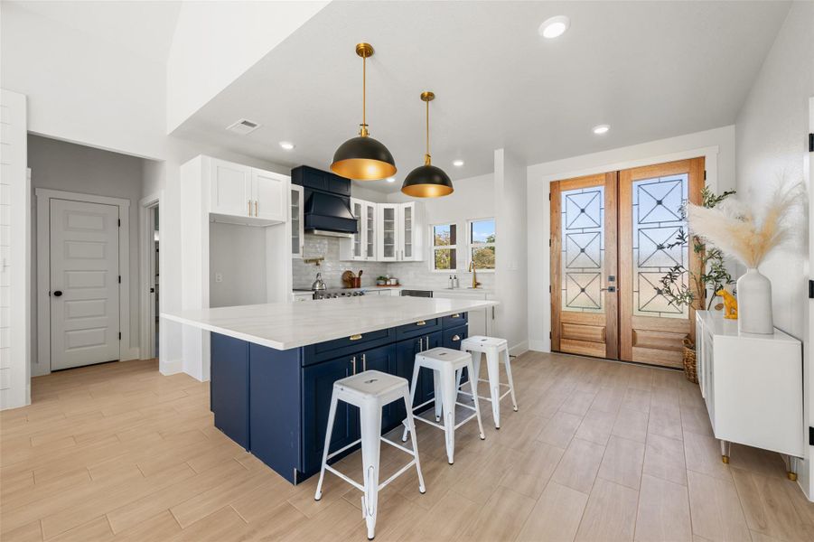 Kitchen featuring blue cabinets, white cabinetry, glass insert cabinets, a kitchen bar, and pendant lighting