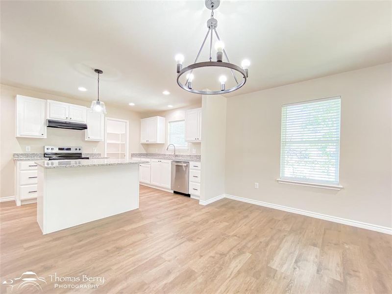 Kitchen with a chandelier, white cabinetry, a kitchen island, light wood-style floors, and decorative light fixtures Kitchen with a chandelier, white cabinetry, a kitchen island, light wood-style floors, and decorative light fixtures