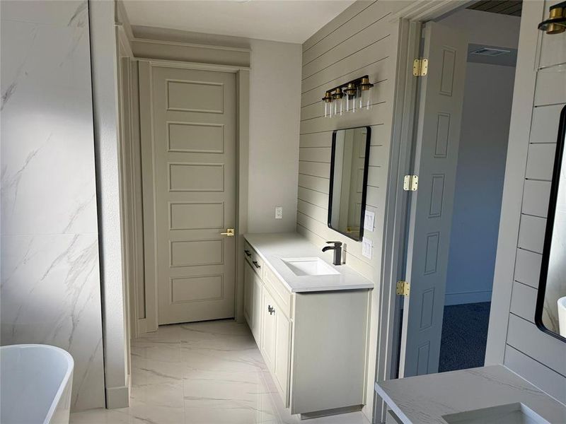 Full bath with vanity, a freestanding tub, and light marble finish floors