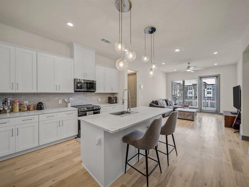 Kitchen featuring open floor plan, white cabinets, a kitchen island with sink, decorative backsplash, and appliances with stainless steel finishes Kitchen featuring open floor plan, white cabinets, a kitchen island with sink, decorative backsplash, and appliances with stainless steel finishes