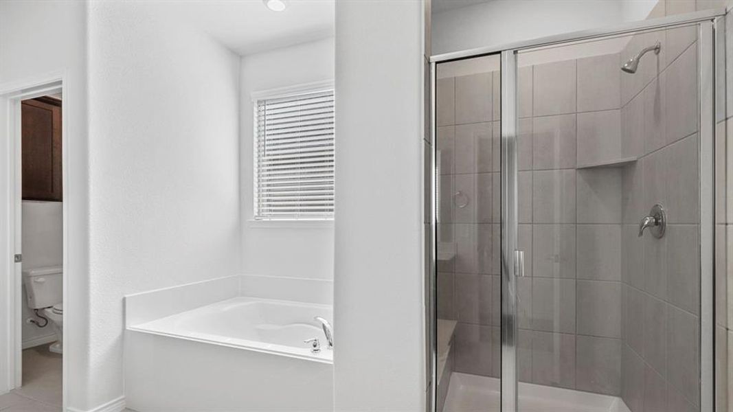 Spacious bathroom featuring a built-in soaking tub, a separate shower with glass enclosure, light grey tile surround, and a recessed shower niche
