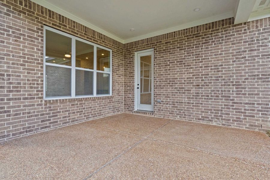Covered patio featuring brick exterior, exposed aggregate concrete flooring, recessed lighting, and a glass-paneled door Covered patio featuring brick exterior, exposed aggregate concrete flooring, recessed lighting, and a glass-paneled door
