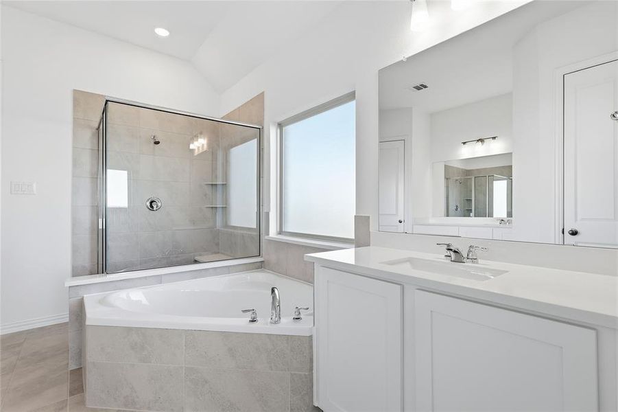 Spacious bathroom featuring a built-in soaking tub, a separate glass-enclosed shower with tiled walls and a built-in bench, and a dual-sink vanity with white cabinetry and a large mirror