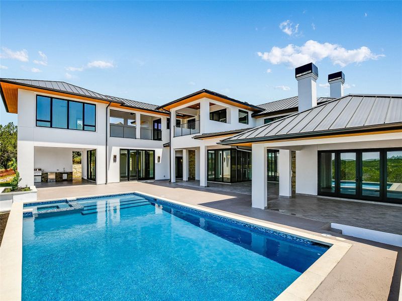 The property features a swimming pool with integrated steps, a patio area, and an outdoor kitchen