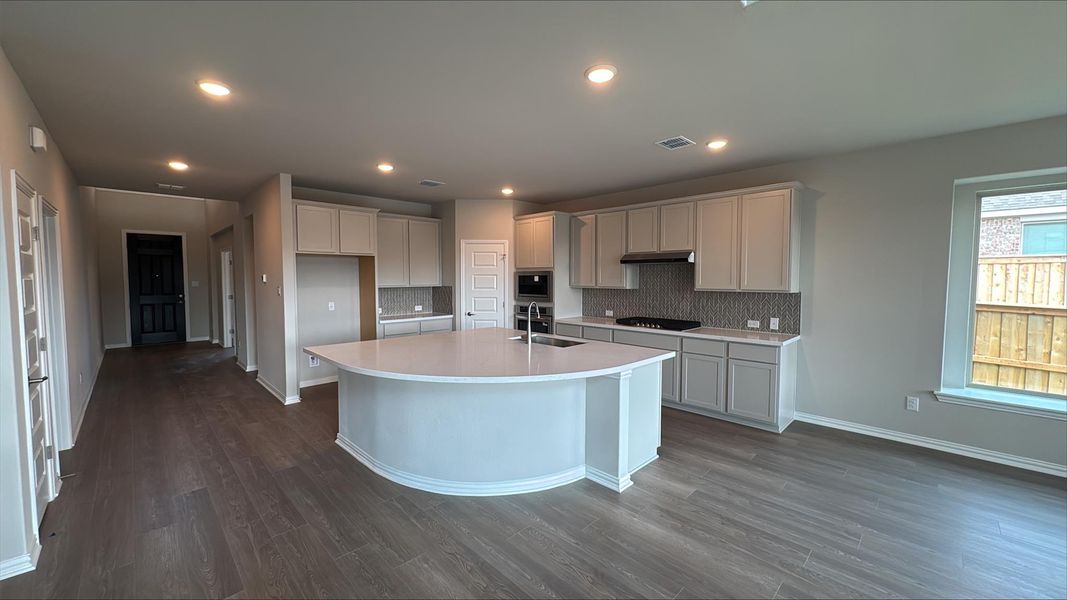 Kitchen featuring dark wood finished floors, a center island with sink, backsplash, recessed lighting, and gas cooktop