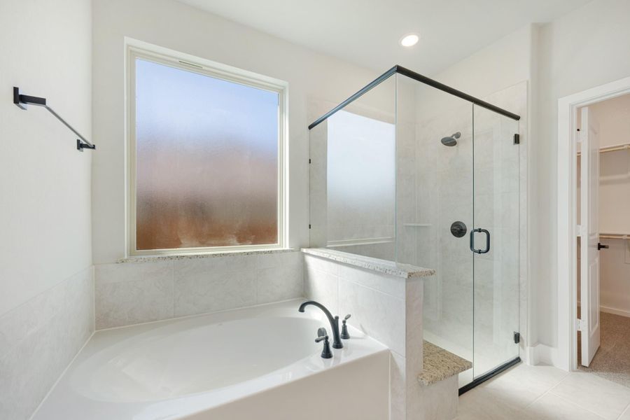 Master bathroom with soaking tub, glass-enclosed shower, and walk-in closet access Master bathroom with soaking tub, glass-enclosed shower, and walk-in closet access