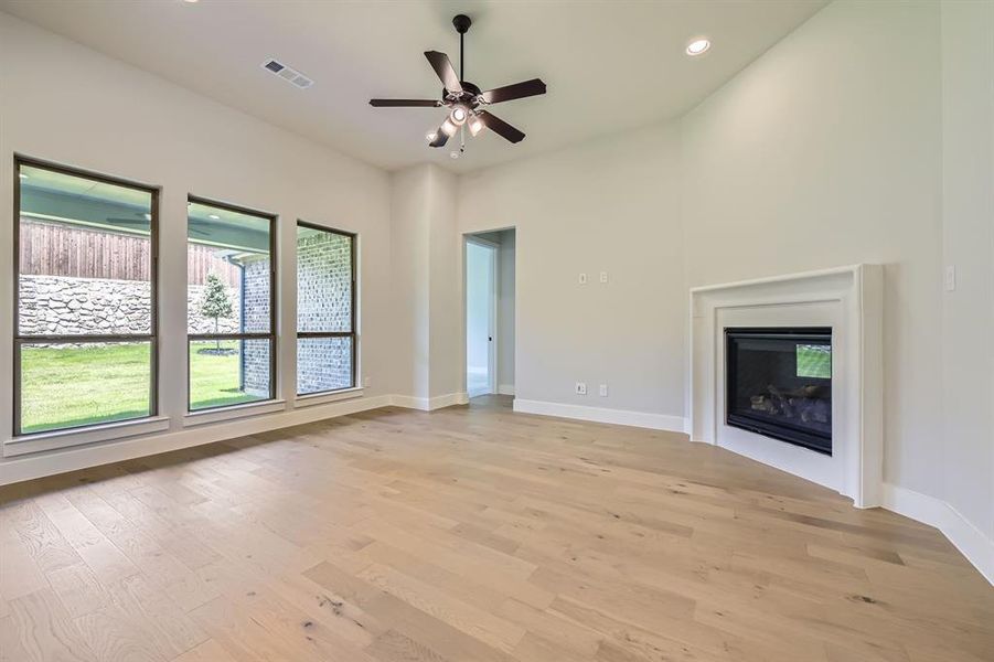 Unfurnished living room with light wood-style flooring, recessed lighting, ceiling fan, and a glass covered fireplace Unfurnished living room with light wood-style flooring, recessed lighting, ceiling fan, and a glass covered fireplace