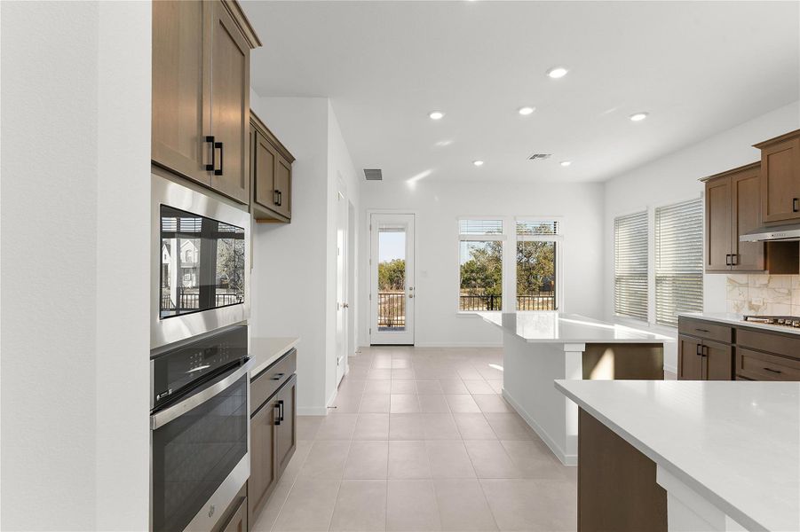 Kitchen with appliances with stainless steel finishes, recessed lighting, light countertops, tasteful backsplash, and under cabinet range hood