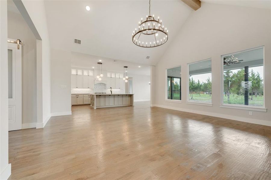 Unfurnished living room featuring light hardwood / wood-style floors, beamed ceiling, a chandelier, high vaulted ceiling, and sink