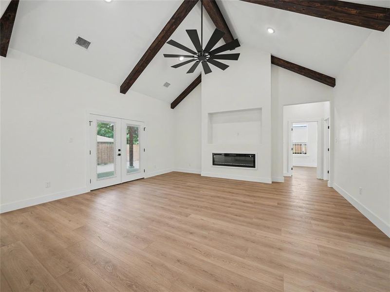 Vaulted ceilings with exposed dark wood beams, contemporary ceiling fan, recessed lighting, integrated linear fireplace, and wood-finish flooring Vaulted ceilings with exposed dark wood beams, contemporary ceiling fan, recessed lighting, integrated linear fireplace, and wood-finish flooring
