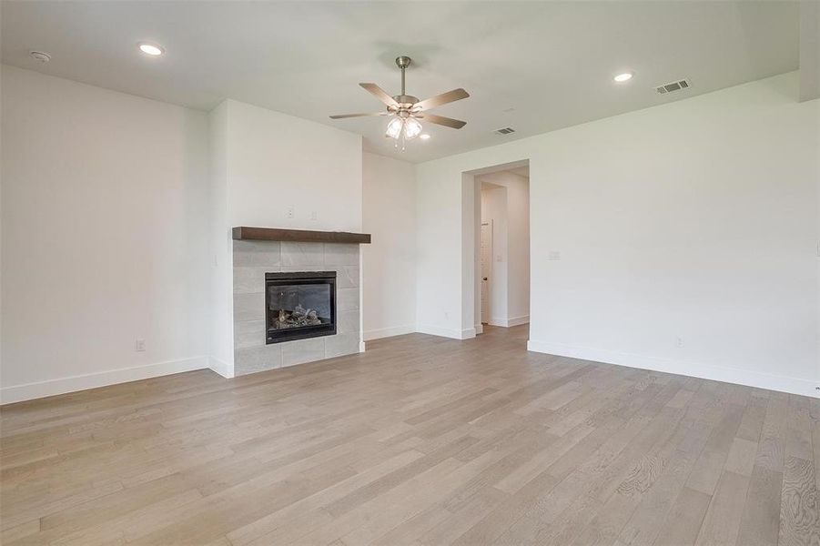 Unfurnished living room with ceiling fan, a tiled fireplace, and light wood-type flooring